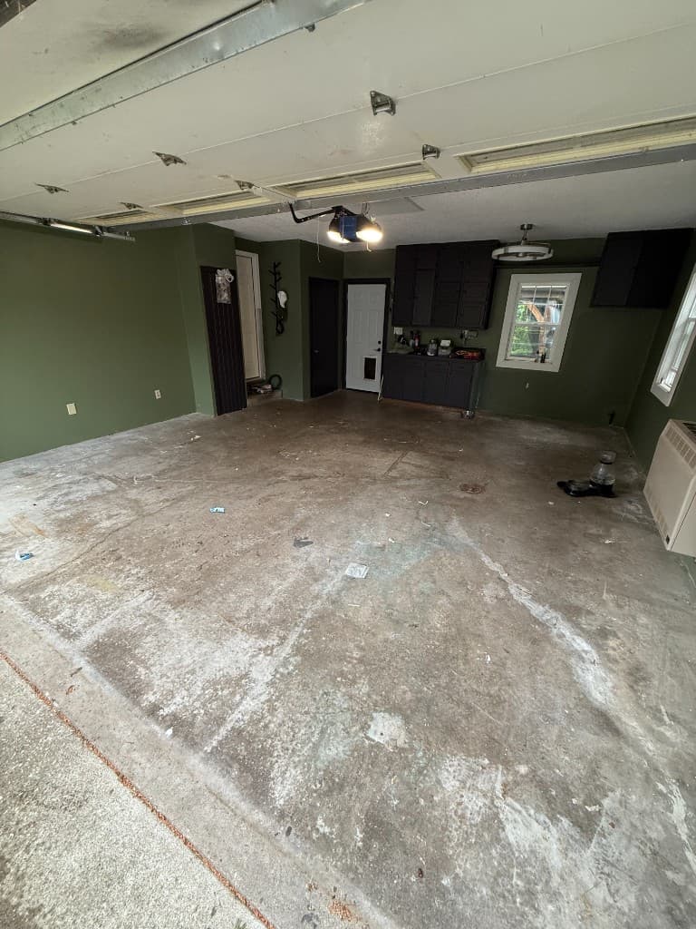 Before coating: peeling stained concrete garage floor with dark green walls.